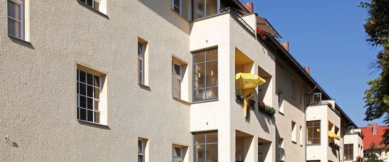 Mehrgeschossiges Wohnhaus von schräg unten, eine Reihe heller Holzfenster über mehrere Geschosse.